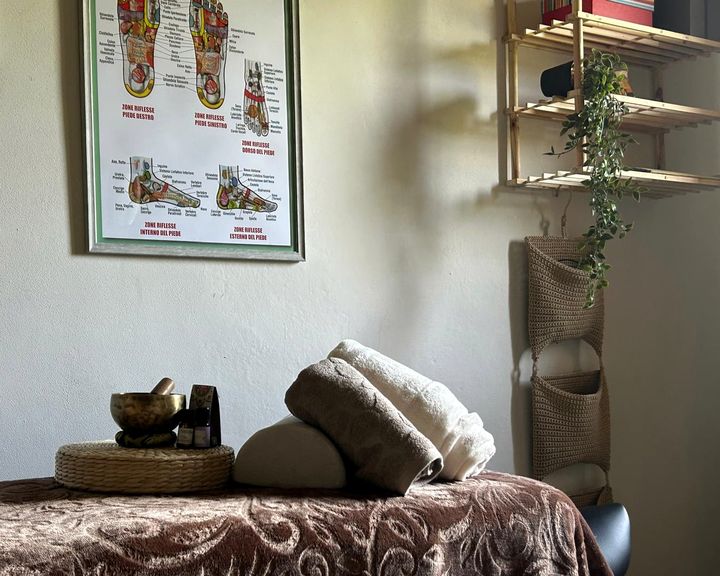 Asciugamani, cuscino, campana tibetana e oli essenziali sul lettino, sotto la tavola delle zone riflesse del piede.