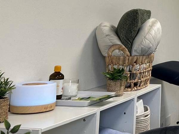Diffusore di aromi, bottiglia di olio, candela, piante e cuscini in una cesta.
