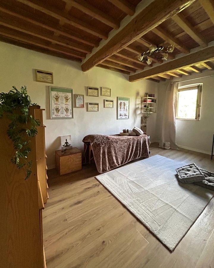 Stanza dei trattamenti con travi in legno, lettino, tappeto e una finestra sul verde.